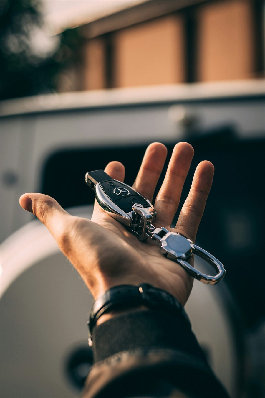 A hand holding car keys in front of a car at golden hour