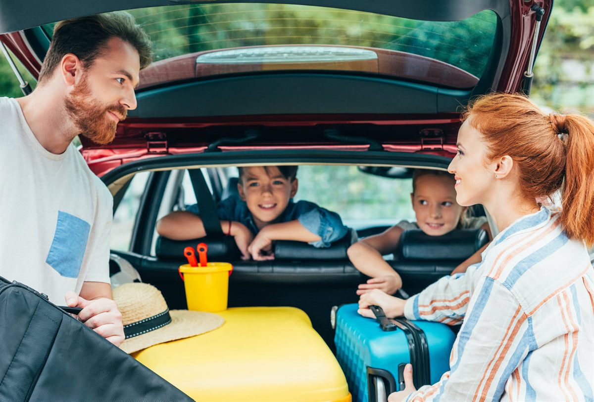 A family loading luggage into a rental car before a holiday road trip